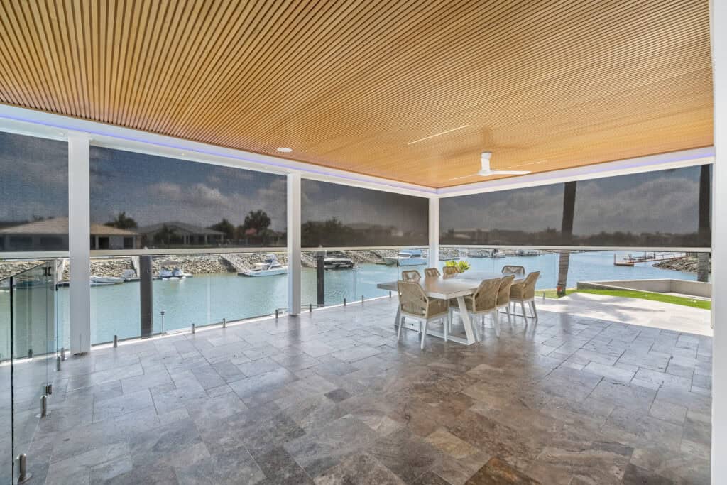 Covered patio with tiled floor, wooden ceiling, ceiling fan, dining table for six, glass railing, and a scenic view of a Cleveland marina with boats and waterfront homes.