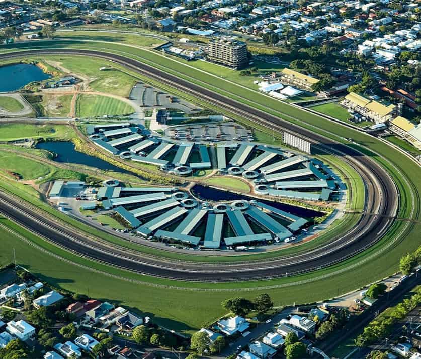 Aerial view of a large horse racing track in Shailer Park with stables arranged in a semi-circular pattern inside the course, surrounded by residential and green areas.