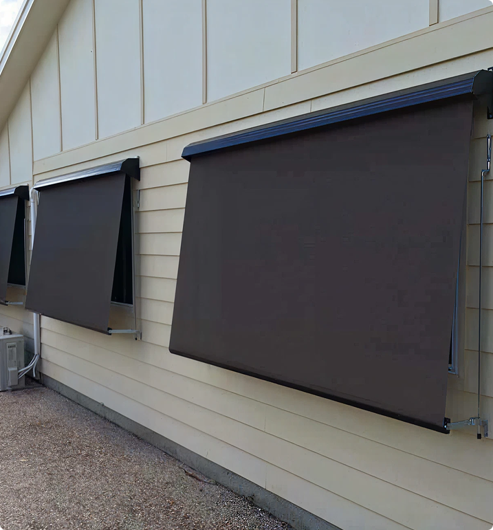 Three large, dark retractable awnings are extended over windows on the side of a beige building with horizontal siding.