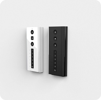 Two wall-mounted remote control panels, one white and one black, each with buttons for navigation and numbered keys, against a plain light background.
