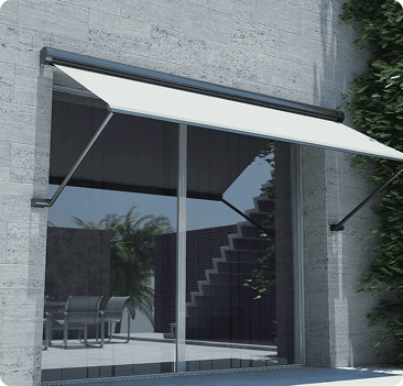 White retractable awning extends over a large glass sliding door on a modern gray stone building, with plants and outdoor furniture visible nearby.