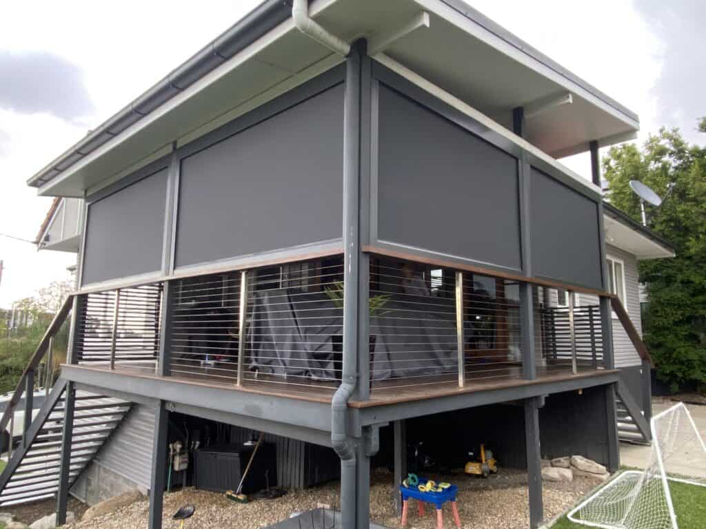 A modern elevated Marsden house with a covered balcony enclosed by dark privacy screens and metal railings, featuring gravel and storage space underneath.