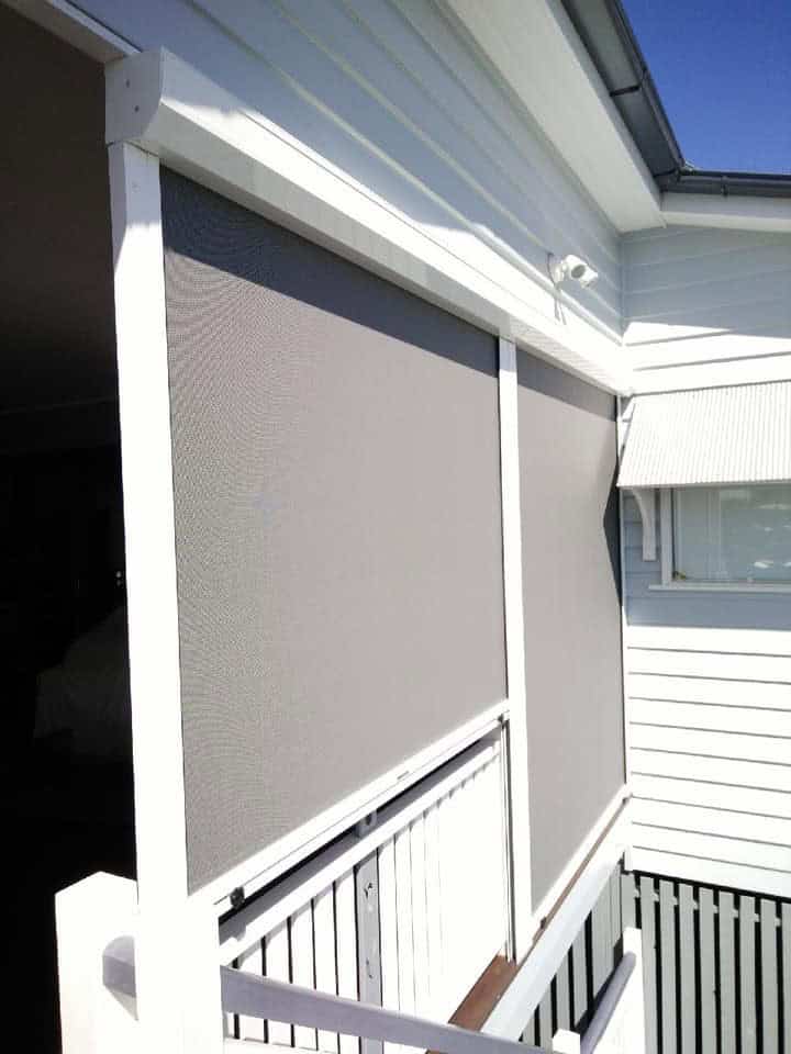 Outdoor area of a white house in North Lakes with two large grey mesh screens installed on a balcony, providing shade and privacy.