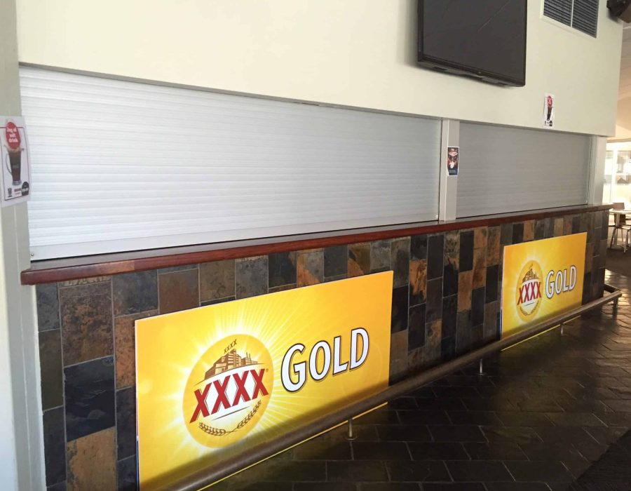 Golf-Club-Bar-04a A closed bar counter with two large XXXX GOLD beer advertisements and metal shutters drawn down over the serving area.