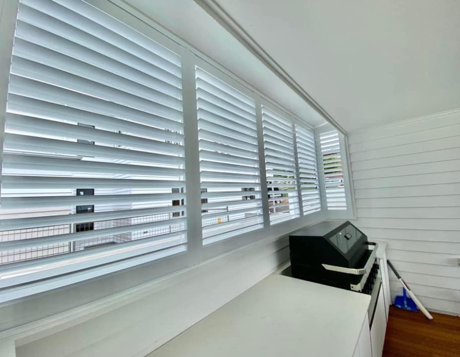 A bright room with indoor PVC shutters covering the windows. Below them, a white counter complements the sleek black cabinet. The wall is lined with white panels, beautifully contrasting the dark wood floor.