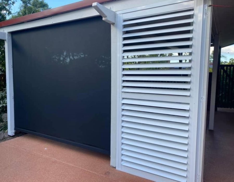 A patio area features a black retractable screen and sleek white louvered panel, complemented by outdoor aluminium shutters. Trees and plants add a lush backdrop, while the ground is elegantly paved with brown concrete.