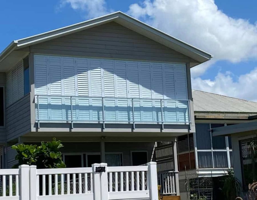 Modern house with aluminum shutters, balcony, and white fence.